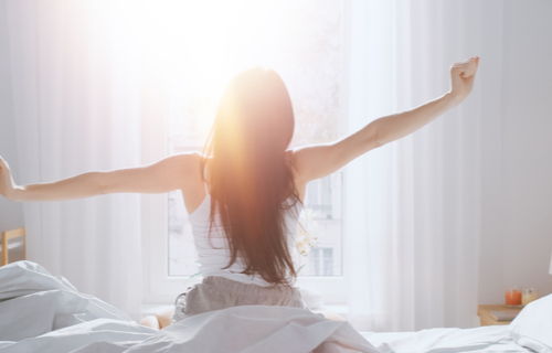 Woman Sitting Up On Bed and Stretching